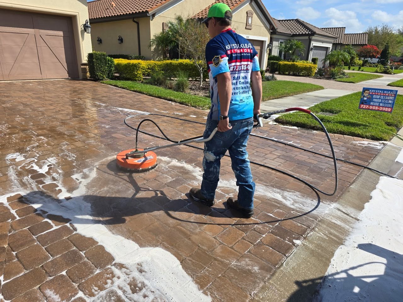 A worker using a surface cleaner on a paver driveway.